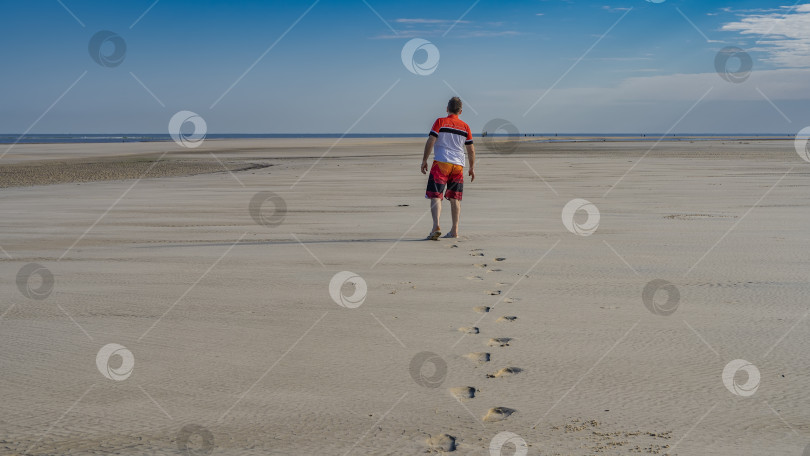 Скачать Океанское дно обнажалось во время отлива. Мужчина идет по мокрому песку. фотосток Ozero