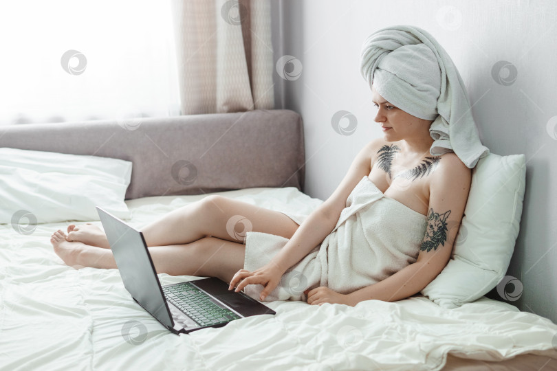 Скачать Тверь, Россия - 2 августа 2021 года. Татуированная женщина после душа лежит на диване с ноутбуком. фотосток Ozero