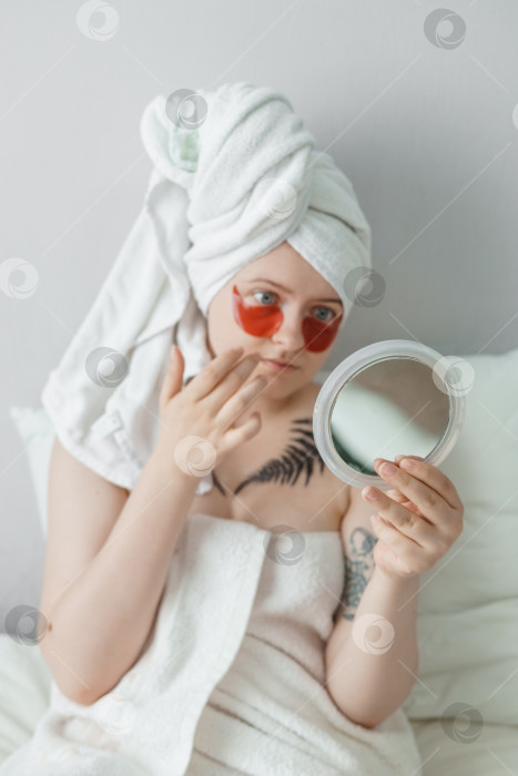 Скачать Тверь, Россия - 2 августа 2021 года Женщина в татуировках после душа лежит на диване с маской для глаз и одновременно смотрится в зеркало. фотосток Ozero