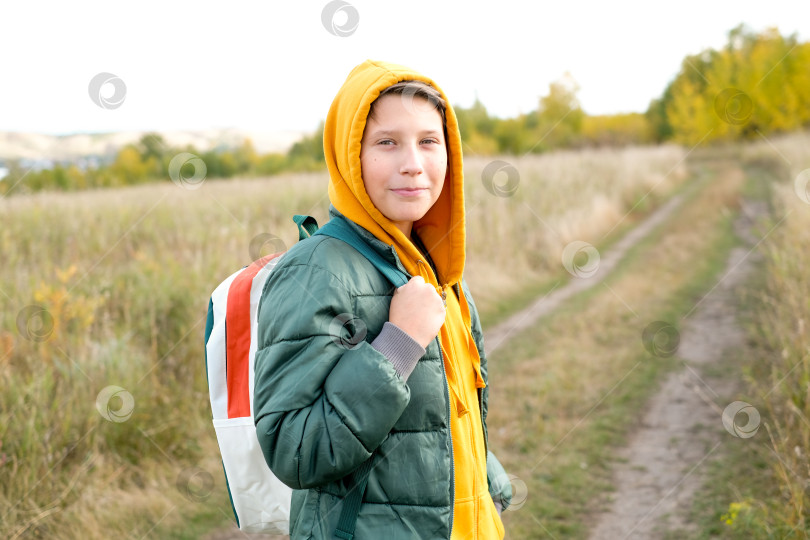 Скачать Портрет жизнерадостного подростка, идущего в школу осенью. Мальчик в желтом капюшоне смотрит в камеру фотосток Ozero