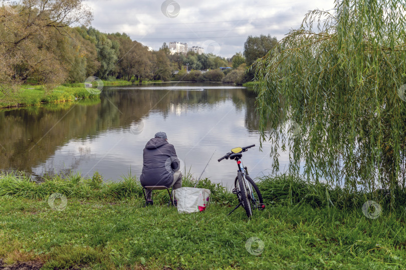 Скачать Рыбак сидит на берегу городского  пруда фотосток Ozero