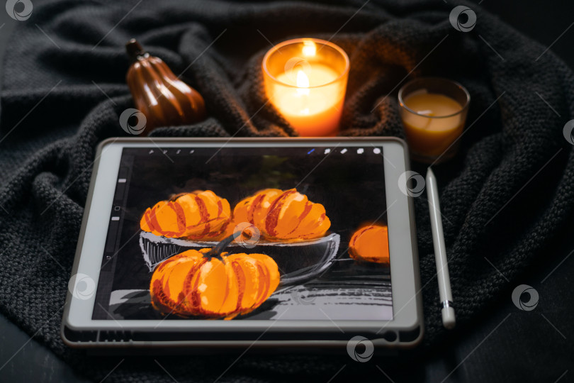 Скачать Натюрморт с тыквами, нарисованный на электронном планшете рядом с горящей свечой и керамической фигуркой тыквы на черном столе. Концепция вдохновения, творчества, саморазвития, хобби, современного искусства. Хэллоуин, день благодарения фотосток Ozero