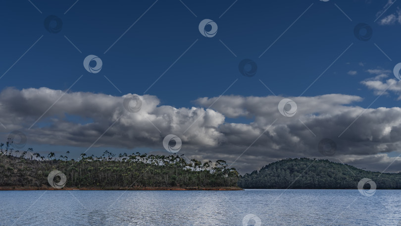 Скачать На холмистых берегах голубого спокойного озера растет лес. фотосток Ozero