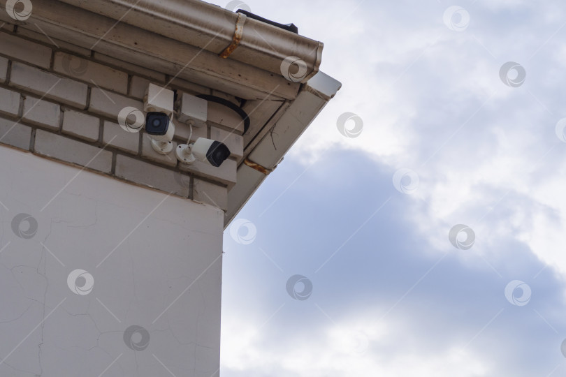 Скачать Камеры наружного наблюдения на старой стене под навесом крыши на фоне голубого неба. Наружное видеонаблюдение, камеры слежения фотосток Ozero