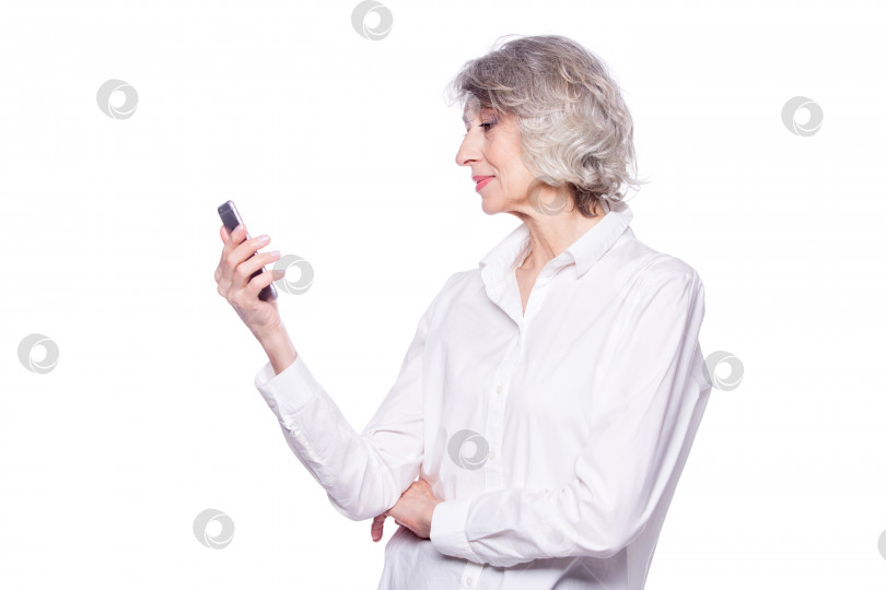 Скачать Красивая зрелая седовласая женщина улыбается с помощью смартфона, просматривая видео или общаясь в чате, изолированные на белом фоне фотосток Ozero