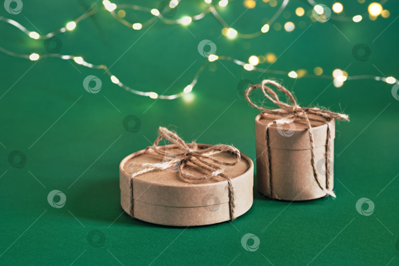Скачать Рождественские устойчивые круглые подарочные коробки и сияющая гирлянда на зеленом фоне. Рождество без отходов фотосток Ozero