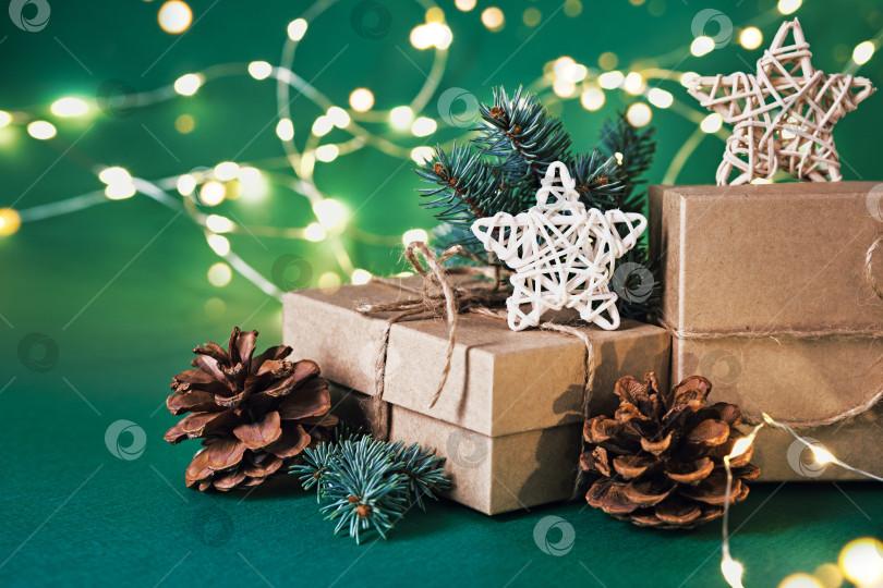 Скачать Рождественские экологически чистые подарочные коробки с натуральным декором и сияющей гирляндой на зеленом фоне. Рождество без отходов фотосток Ozero