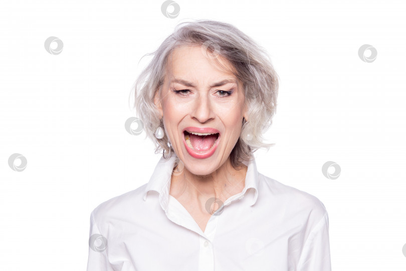 Скачать Фотография зрелой красивой седовласой женщины, громко кричащей и кричащей с широко открытым ртом с сердитым выражением лица, выделенным на белом фоне фотосток Ozero