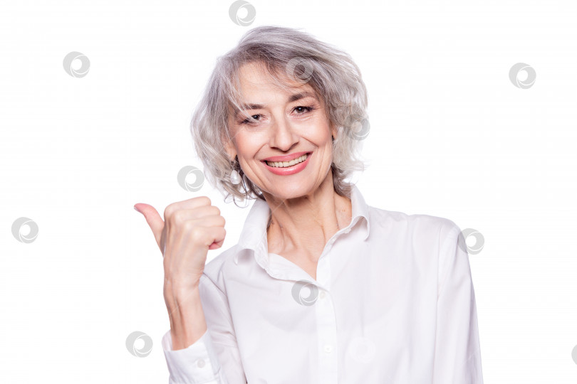 Скачать Крупным планом портрет счастливой улыбающейся зрелой женщины лет шестидесяти с модными седыми волосами, делающей поднятый вверх большой палец, выражающий одобрение, изолированный на белом фоне фотосток Ozero