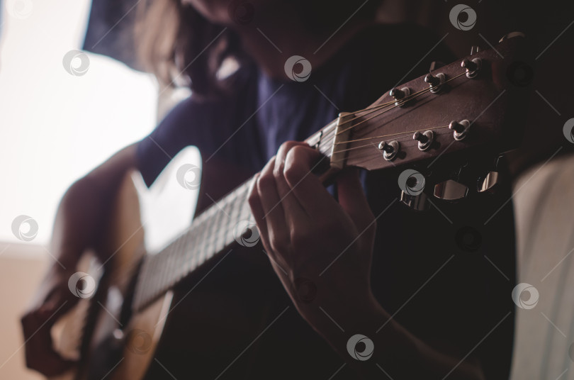 Скачать Девушка играет на гитаре в комнате.Тусклый свет из окна фотосток Ozero