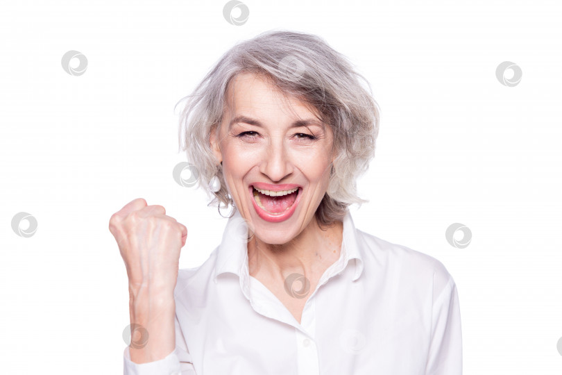 Скачать Портрет веселой счастливой пожилой женщины, громко кричащей и демонстрирующей победу поднятым кулаком, выделенный на белом фоне фотосток Ozero