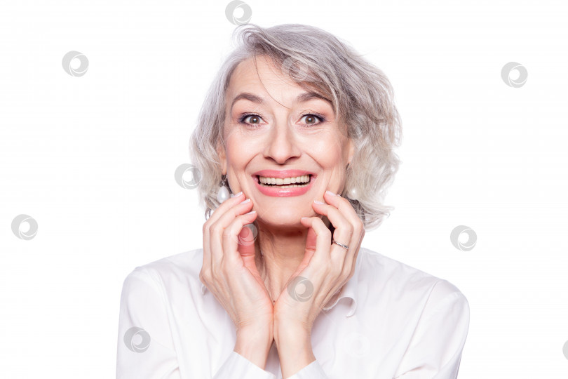 Скачать Портрет привлекательной зрелой женщины, смотрящей в камеру с красивой широкой улыбкой и руками на лице, удивленной и шокированной, изолированной на белом фоне фотосток Ozero