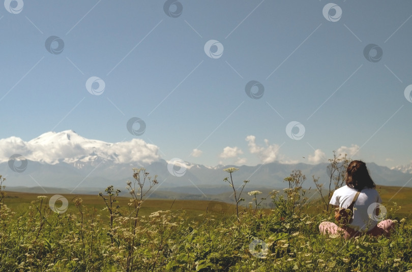 Скачать Девушка сидит на лугу и смотрит на прекрасный горный пейзаж. фотосток Ozero