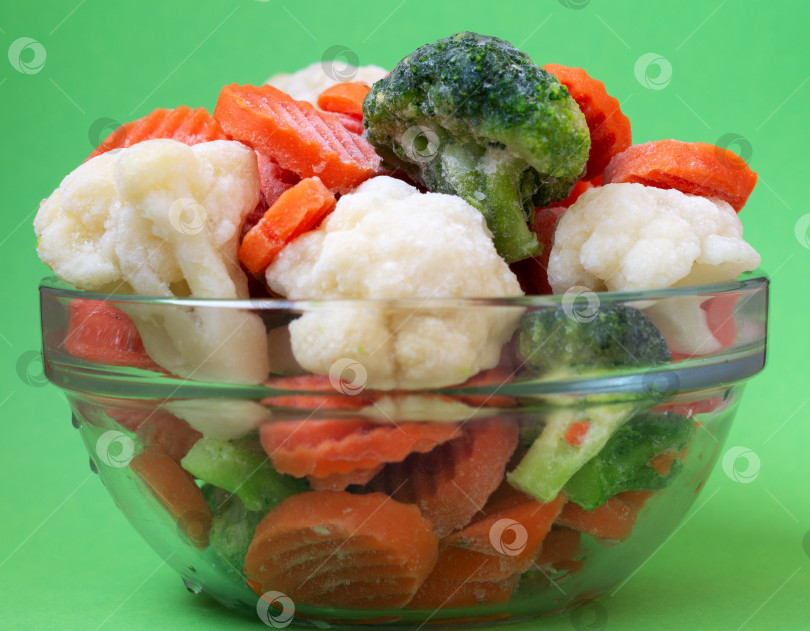 Скачать Замороженные овощи брокколи и морковь в стеклянной тарелке на зеленом фоне. фотосток Ozero