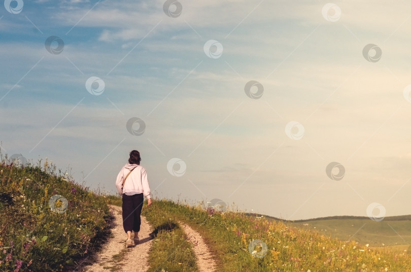 Скачать Девушка идет по проселочной дороге вдоль горного хребта на фоне голубого неба. фотосток Ozero