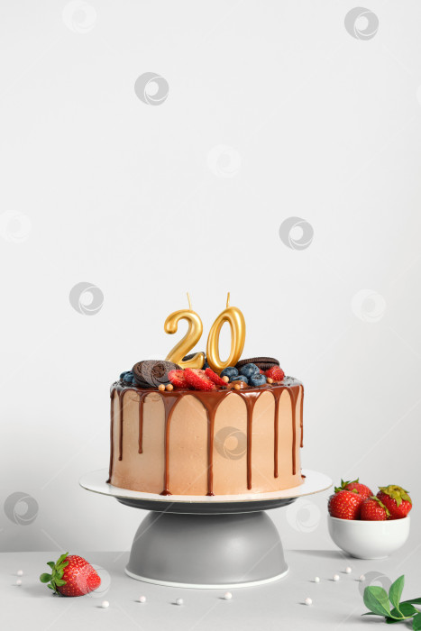 Скачать Шоколадный праздничный торт с ягодами, печеньем и двадцатью золотыми свечами на белом фоне, место для копирования фотосток Ozero