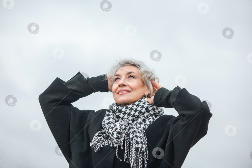Скачать Портрет свободной, независимой и счастливой зрелой женщины в теплой одежде на фоне серого осеннего неба фотосток Ozero