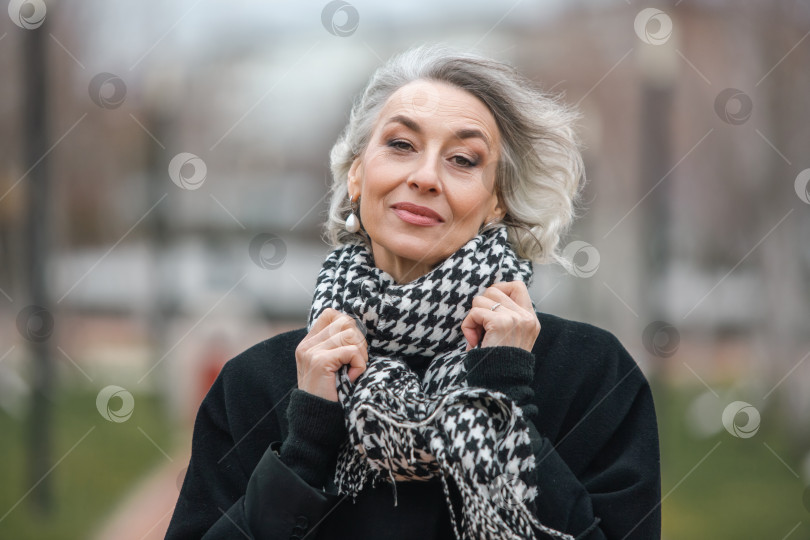 Скачать Портрет свободной и независимой взрослой женщины в модном шарфе, прогуливающейся по холодному осеннему парку фотосток Ozero