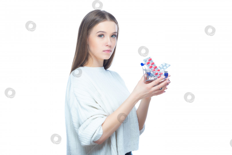Скачать Студийный снимок молодой женщины, держащей в руках небольшую тележку для покупок, полную таблеток, таблеток и лекарств, выделенных на белом фоне фотосток Ozero