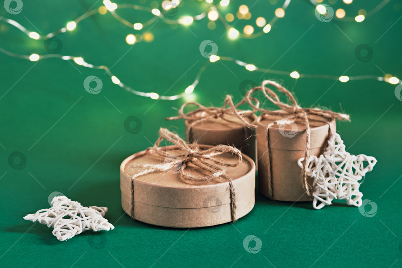 Скачать Рождественские устойчивые круглые подарочные коробки и сияющая гирлянда на зеленом фоне. Рождество без отходов фотосток Ozero