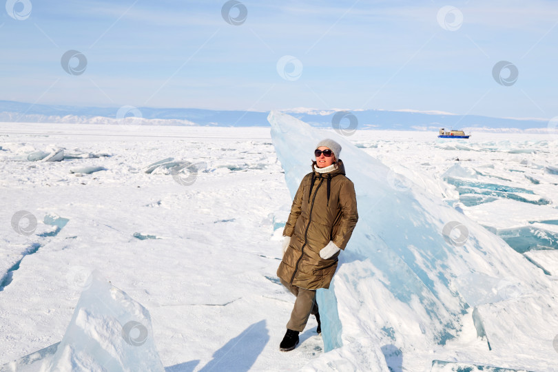 Скачать Молодая женщина стоит у огромной глыбы прозрачного голубого льда. фотосток Ozero