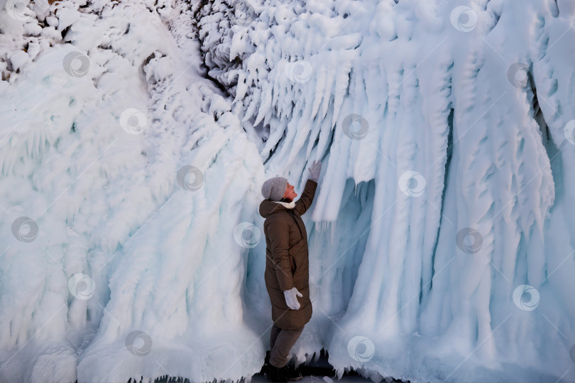 Скачать Женщина смотрит на огромные сосульки на скалах острова Олтрек. Зимнее путешествие по озеру Байкал. фотосток Ozero