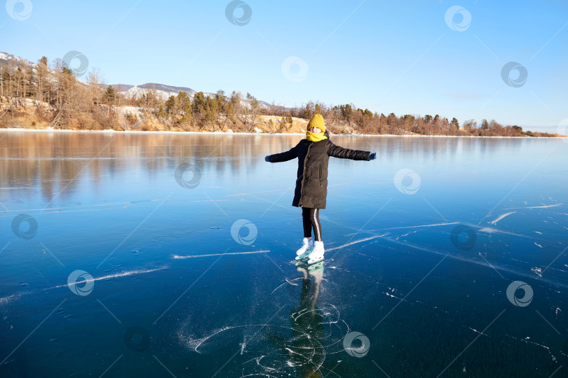 Скачать Молодая счастливая девушка катается на коньках по прозрачному льду замерзшего озера Байкал солнечным зимним днем. фотосток Ozero