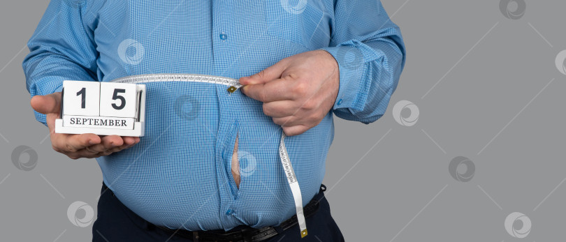 Скачать толстяк измеряет размер живота сантиметровой рулеткой. рубашка была порвана из-за больших жировых отложений. 15 сентября, День похудения. люди страдают от лишнего веса. фотосток Ozero