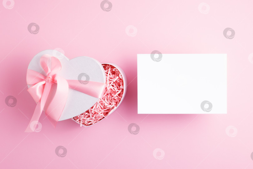 Скачать Реклама, рекламный праздничный макет с пустой открыткой и красивой праздничной подарочной коробкой в форме сердца на светло-розовом фоне. фотосток Ozero