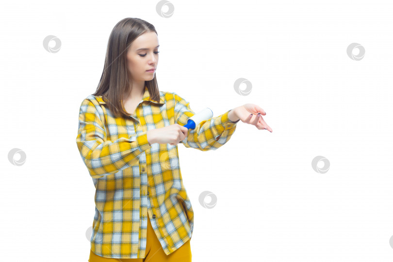 Скачать Портрет молодой женщины, использующей средство для удаления ворса, чтобы очистить желтую клетчатую рубашку от пыли, волос, ворса и пуха, выделенный на белом фоне фотосток Ozero