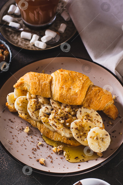 Скачать Бутерброд с круассаном с бананом, медом и орехами на тарелке на столе вертикальный вид фотосток Ozero