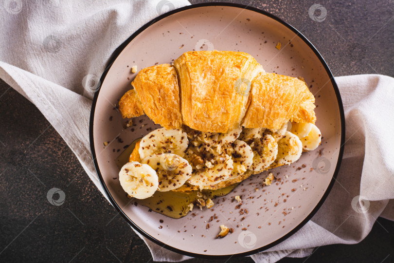 Скачать Крупный план круассана с бананом, медом, шоколадом и орехами на тарелке на столе вид сверху фотосток Ozero