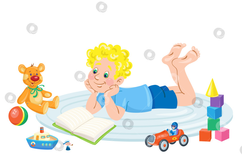 Скачать Маленький забавный мальчик лежит на ковре и читает книжку, окруженный игрушками. фотосток Ozero