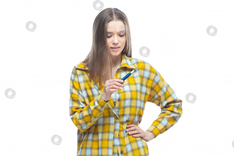 Скачать Портрет молодой женщины в желтой клетчатой рубашке, смотрящей на электронную сигарету в руках, выделенную на белом фоне фотосток Ozero