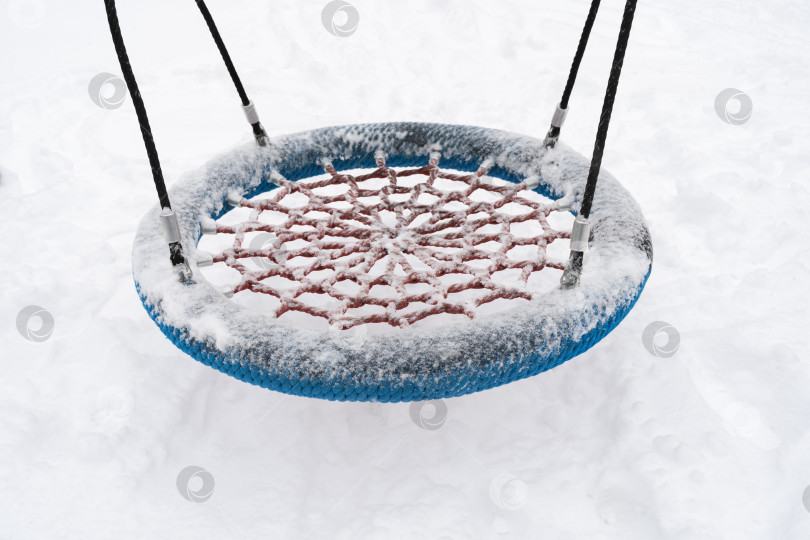 Скачать Круглое гнездо типа качелей на детской площадке покрыто снегом. фотосток Ozero