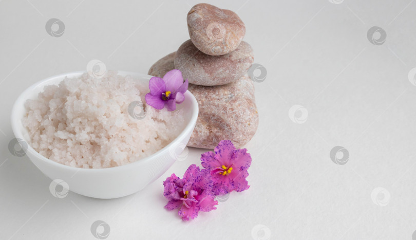 Скачать Розовая крупная соль в белой миске стоит на белом фоне рядом с розовыми камнями и розово-фиолетовыми цветами фотосток Ozero