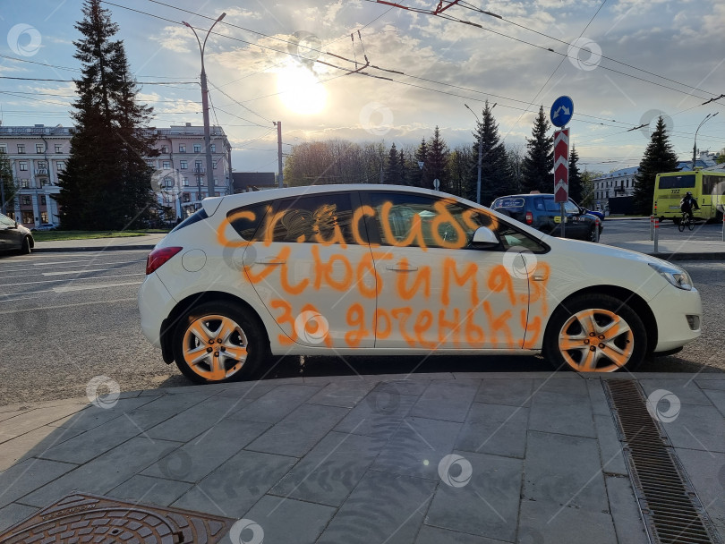 Скачать разрисованный оранжевой краской белый автомобиль с надписью "Спасибо, любимая, за доченьку", припаркованный около тротуара фотосток Ozero