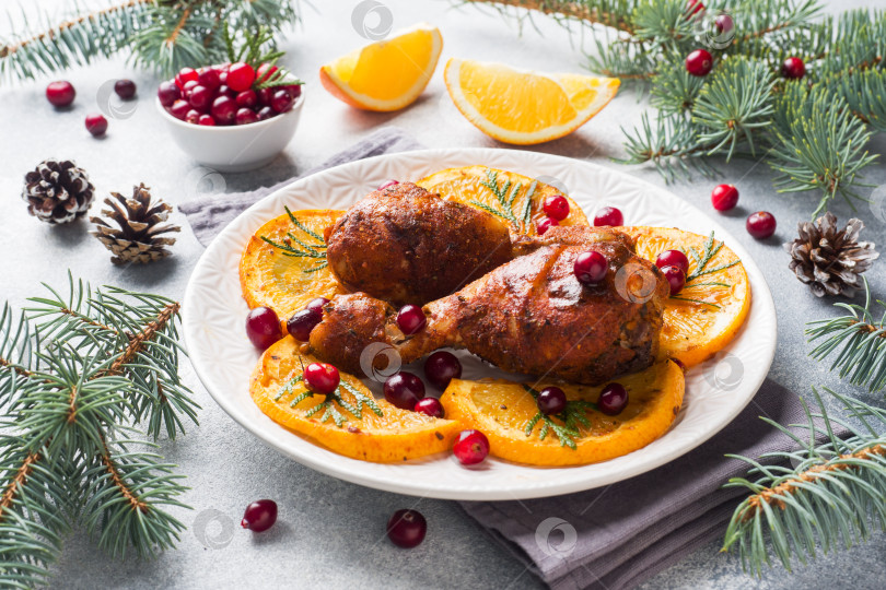 Скачать Запеченная куриная голень с апельсинами и клюквой на светло-сером фоне тарелки. Рождественский праздничный стол с украшениями. фотосток Ozero