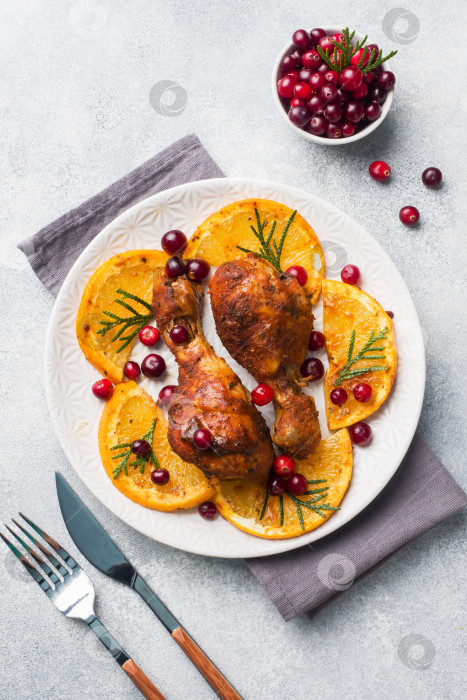 Скачать Запеченная куриная голень с апельсинами и клюквой на светло-сером фоне тарелки. Рождественский праздничный стол с украшениями. Пространство для копирования. фотосток Ozero