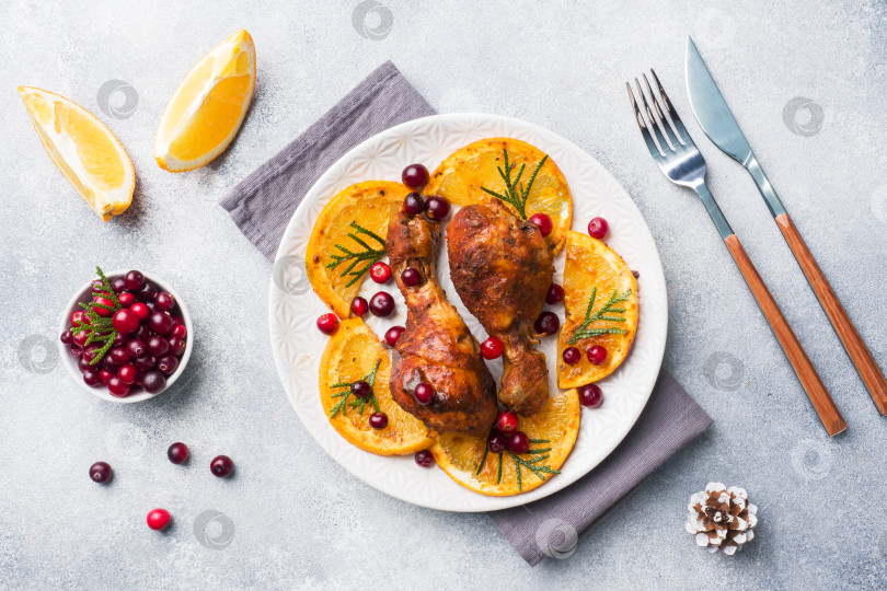 Скачать Запеченная куриная голень с апельсинами и клюквой на светло-сером фоне тарелки. Рождественский праздничный стол с украшениями. Пространство для копирования. фотосток Ozero