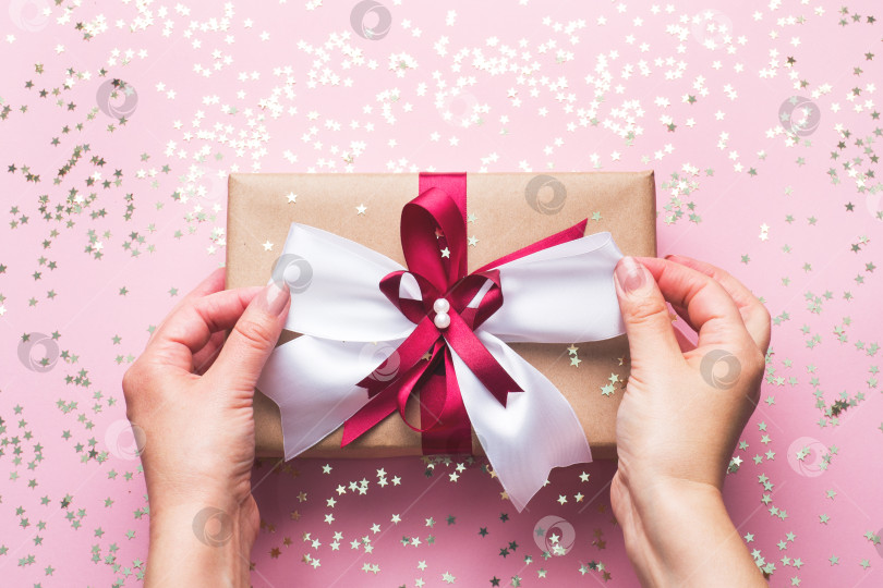 Скачать Подарок или подарочная коробка с большим бантом в руках женщины на розовом столе. Композиция Flatlay на Рождество, день рождения, день матери или свадьбу. фотосток Ozero