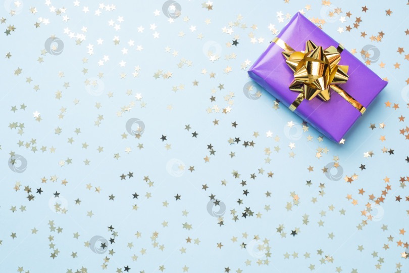Скачать Плоский фон для празднования Рождества и Нового года. Подарочные коробки фиолетового цвета с бантиками из золотых лент и звездочками из конфетти на синем фоне. пространство для копирования вида сверху. фотосток Ozero