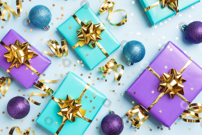 Скачать Плоский фон для празднования Рождества и Нового года. Подарочные коробки фиолетового и бирюзового цветов с бантиками из золотых лент и звездочками из конфетти на синем фоне. вид сверху фотосток Ozero