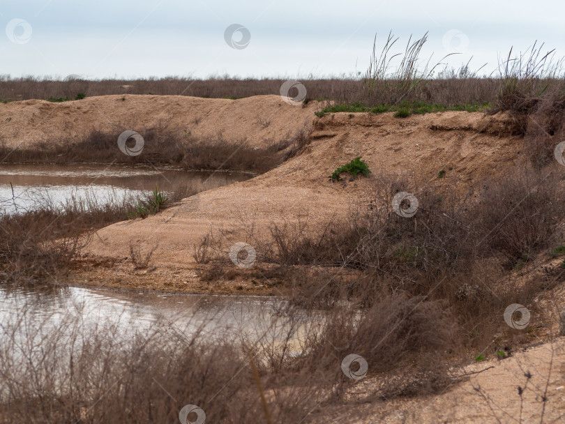 Скачать Вода в песчаной яме. Заброшенный ракушечный карьер, затопленный водой и сухой травой. Охрана окружающей среды. Пейзаж заброшенного карьера выглядит ужасно фотосток Ozero