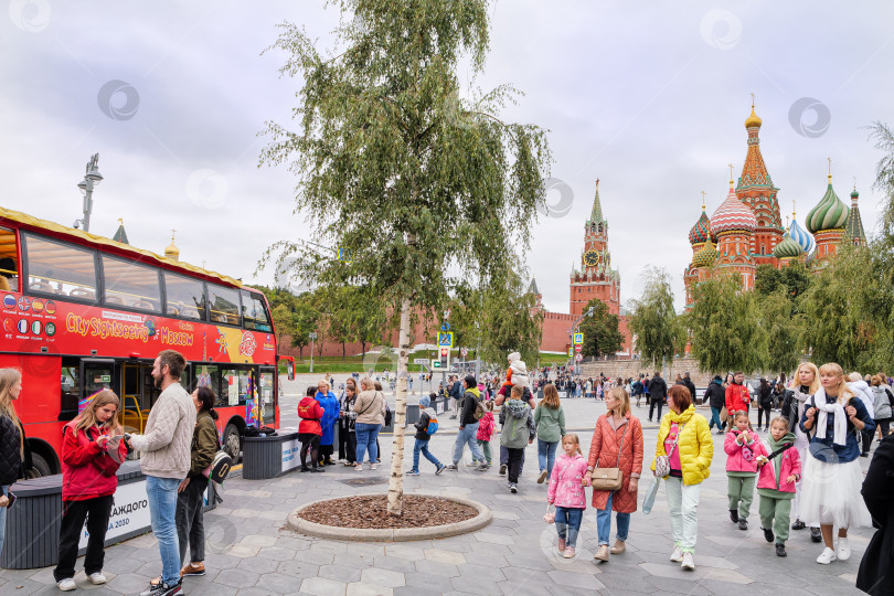 Скачать Москва. Гуляющие люди и красный экскурсионный автобус на фоне Московского Кремля. фотосток Ozero