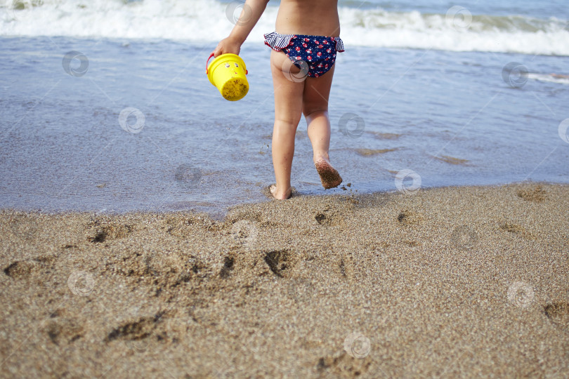 Скачать Маленькая девочка бежит по пляжу к морю. Следы детских ножек на песке. фотосток Ozero