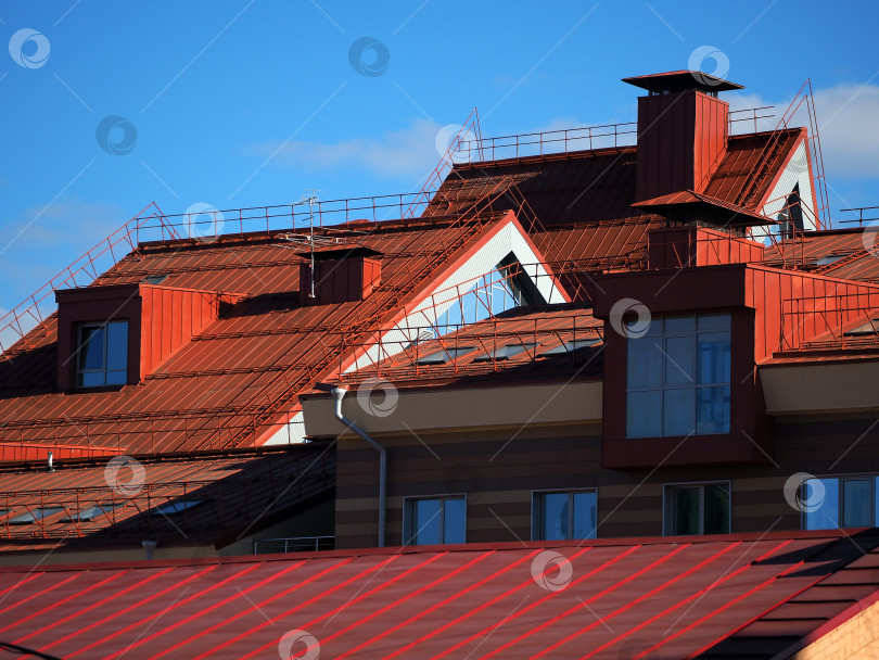 Скачать Скатные крыши домов покрыты кровельным железом. Крыши домов прижаты друг к другу. На красных крышах видны вентиляционные трубы, ограждения и окна. фотосток Ozero