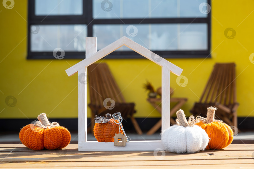 Скачать Осенний декор на крыльце желтого дома снаружи из тыквы, фонаря, гирлянд и фигурки дома и ключа. Вечеринка на Хэллоуин, осеннее настроение, праздник урожая, недвижимость, страхование, ипотека фотосток Ozero