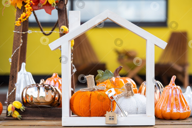 Скачать Осенний декор на крыльце желтого дома снаружи из тыквы, фонаря, гирлянд и фигурки дома и ключа. Вечеринка на Хэллоуин, осеннее настроение, праздник урожая, недвижимость, страхование, ипотека фотосток Ozero