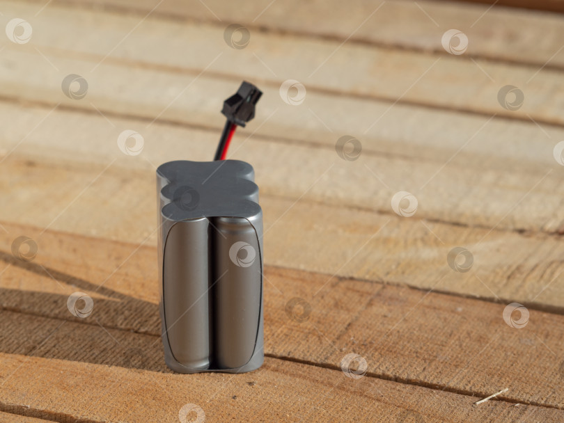 Скачать Литий-ионный аккумулятор крупным планом на деревянном фоне, вид сбоку. Батарейка для радиоуправляемых игрушек фотосток Ozero